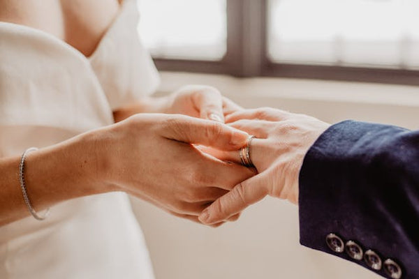 A bride putting a wedding band onto the groom’s finger