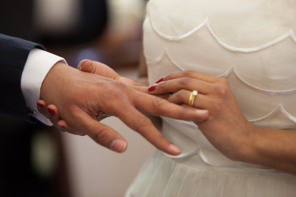 A bride placing a wedding ring on a groom’s left hand